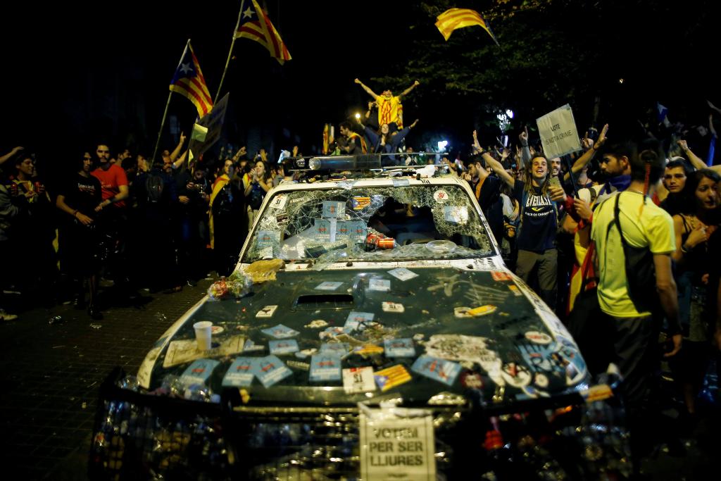 Protesters shout slogans next to a damaged Spanish Civil Guard patrol car outside the Catalan region's economy ministry building