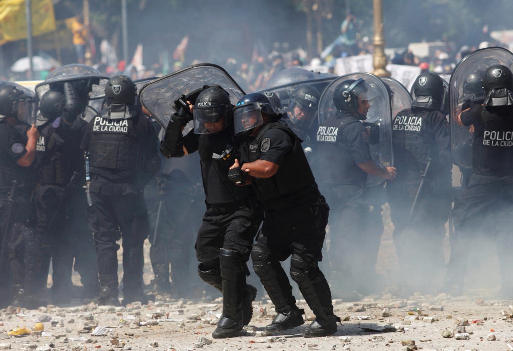 A police officer assists a colleague during clashes with demonstrators as lawmakers debate a pension reform measure, in Buenos A