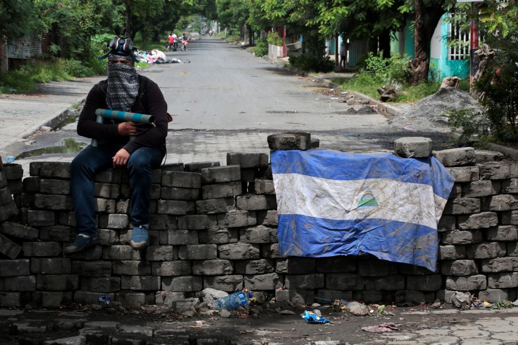 A man holding a homemade mortar sits on a roadblock in Managua