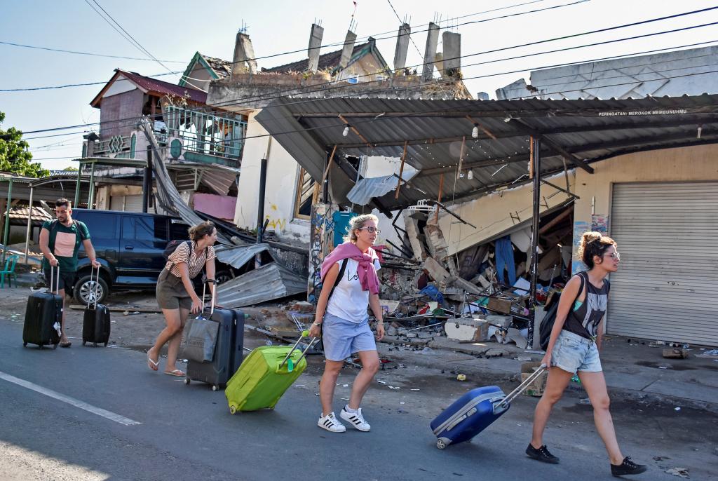 FILE PHOTO - Foreign tourists pull their suitcases as they walk past damaged buildings following a strong earthquake in Pemenang